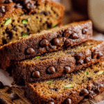 Moist chocolate chip zucchini bread sliced on a wooden board with melted chocolate chips and golden crust