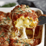 Close-up of cheesy lasagna roll up being lifted from baking dish with marinara and melted mozzarella