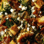 Close-up of roasted broccoli salad with feta cheese, caramelized shallots, beef, and crunchy sourdough croutons.