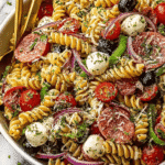 Overhead view of Italian pasta salad with rotini, cherry tomatoes, mozzarella, olives, salami, and red onion in a white bowl.