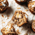Freshly baked apple muffins topped with toasted coconut flakes, cut open to reveal a moist crumb and melting butter