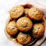 Hand holding a basket lined with parchment and filled with freshly baked lemon poppyseed zucchini muffins.