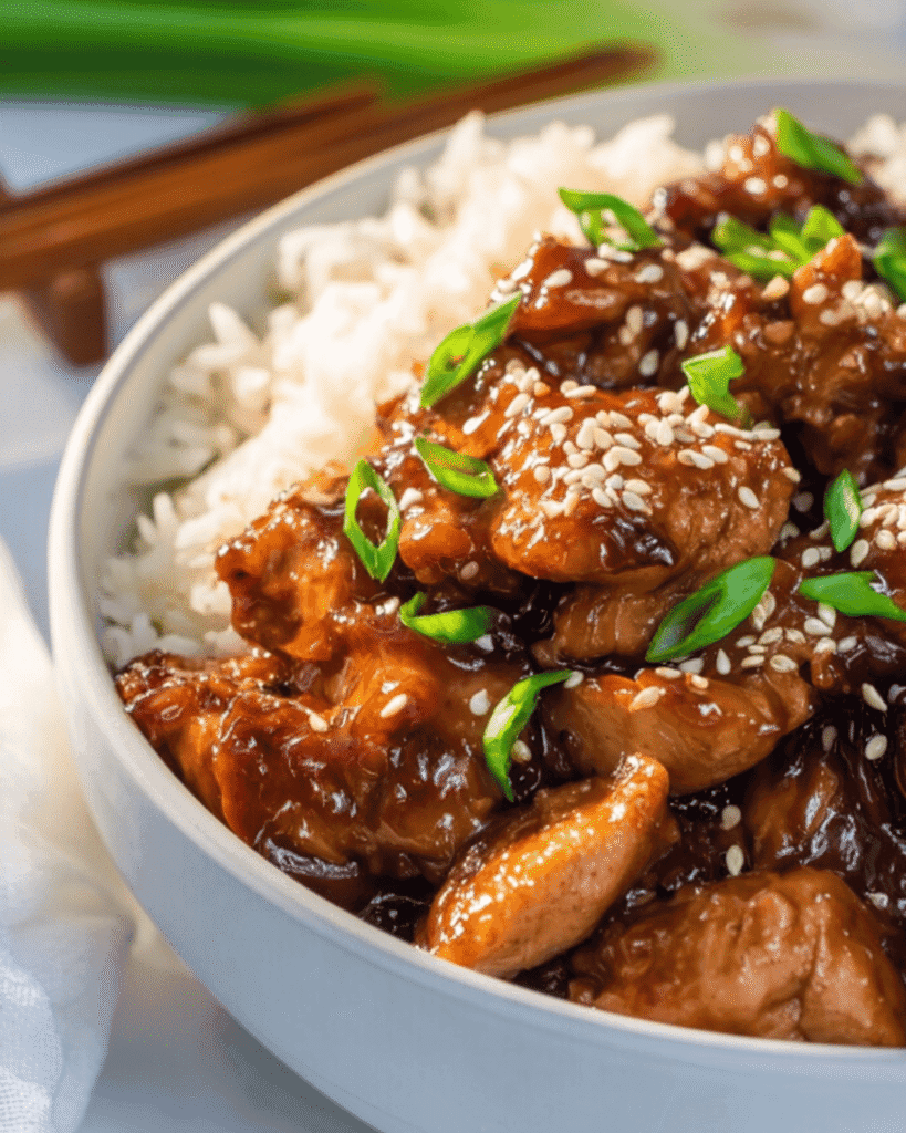 Bowl of ginger chicken with steamed rice, sesame seeds, and green onions.