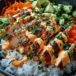 Sliced grilled Bang Bang chicken over white rice, topped with creamy spicy mayo and garnished with avocado, cucumber, shredded carrots, and red peppers.