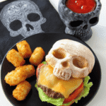 Halloween cheeseburger in a skull-shaped bun served with crispy tater tots and ketchup in a skull-shaped cup