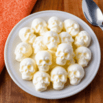Plate of spooky Mozzarella Cheese Skulls for Halloween snacks on a wooden table with an orange napkin