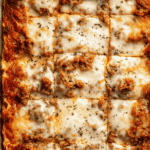 Overhead view of oven baked lasagna cut into squares with melted mozzarella and rich meat sauce.