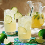 Two tall glasses of chilled lime squash with ice cubes and lime slices, served with stainless steel straws