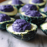 Halloween deviled eggs with green cracked shells and purple filling arranged on a marble plate.