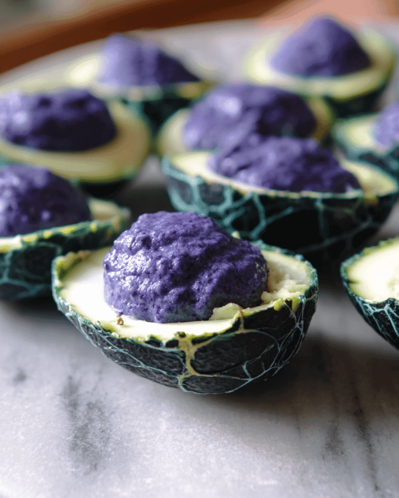 Halloween deviled eggs with green cracked shells and purple filling arranged on a marble plate.