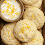 Close-up view of soft chewy lemon cookies coated with sugar and sprinkled with fresh lemon zest beside a wooden bowl of lemon sugar.