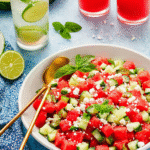 Fresh watermelon cucumber salad with feta and mint served in a white bowl, garnished with herbs, and paired with summer drinks