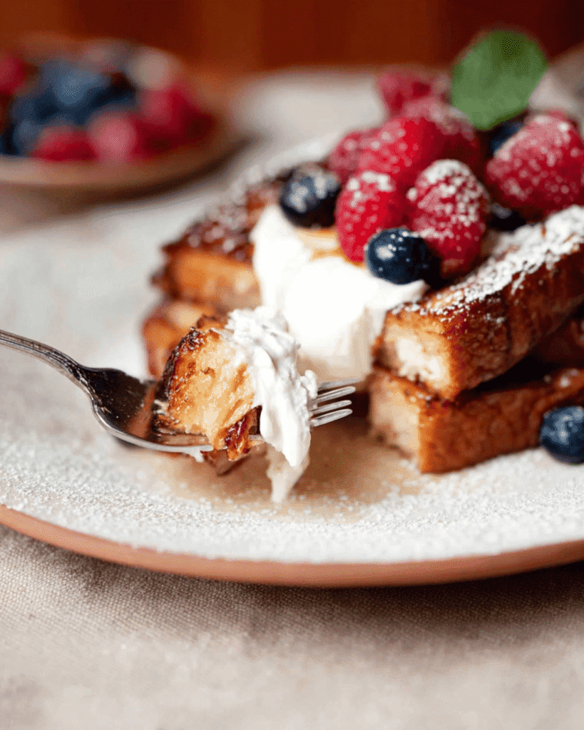 Close-up bite of high protein French toast with whipped cream and berries on a fork