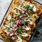 Glass baking dish filled with Black Bean Sweet Potato Enchiladas topped with sour cream, cilantro, and red onion
