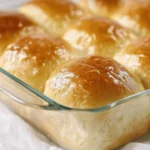 Shiny golden Texas Roadhouse Rolls in a glass dish with buttery glaze