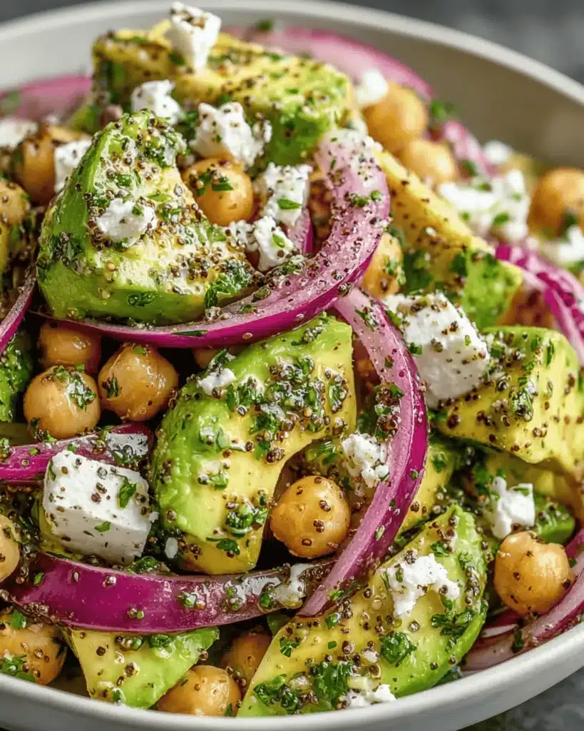 Close-up of creamy avocado chunks, chickpeas, red onions, and feta tossed in lemon herb olive oil dressing