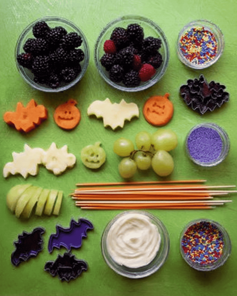 Halloween Fruit Kabobs ingredients including melon, grapes, blackberries, yogurt, sprinkles, skewers, and bat cookie cutters.