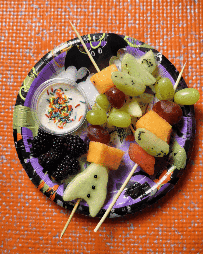Halloween Fruit Kabobs with grapes, melon, blackberries, and yogurt dip on a spooky Halloween plate.