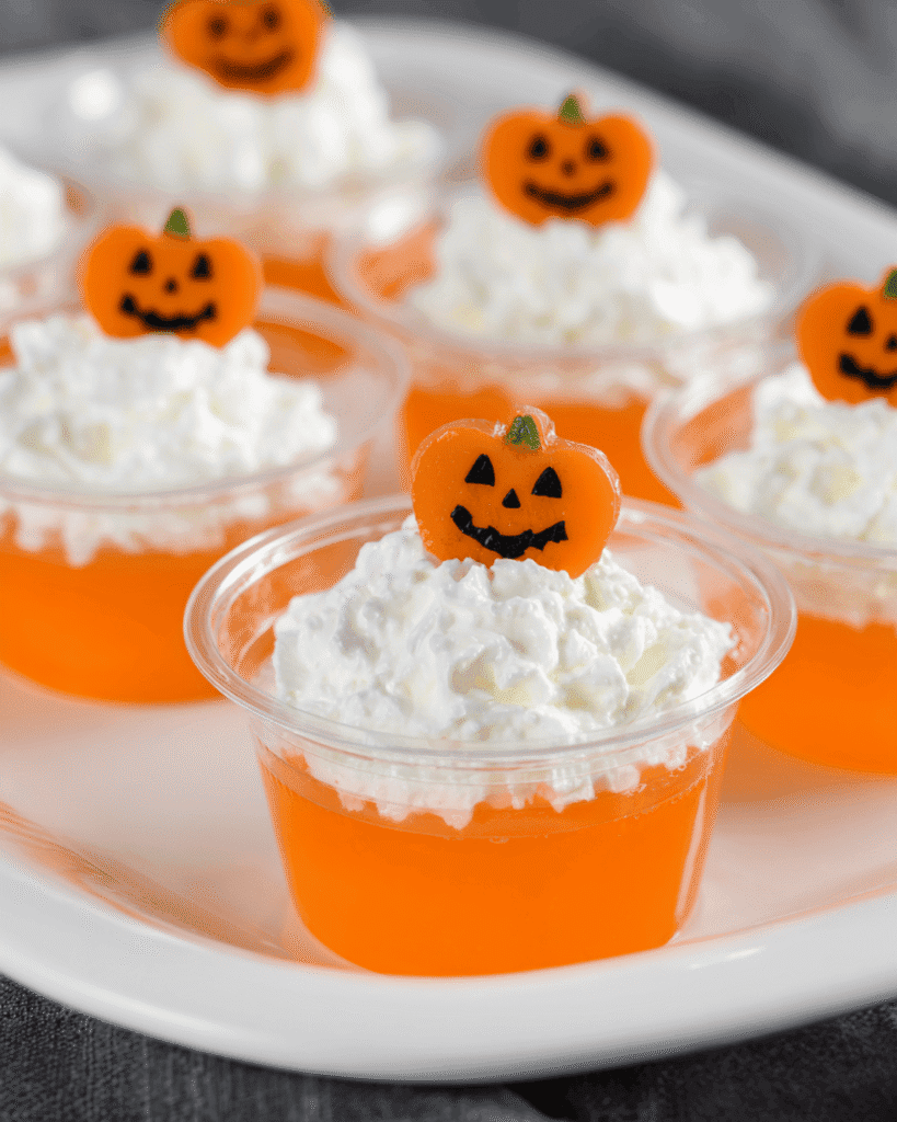 Keto Halloween jello shots with whipped cream and pumpkin toppers on a serving tray