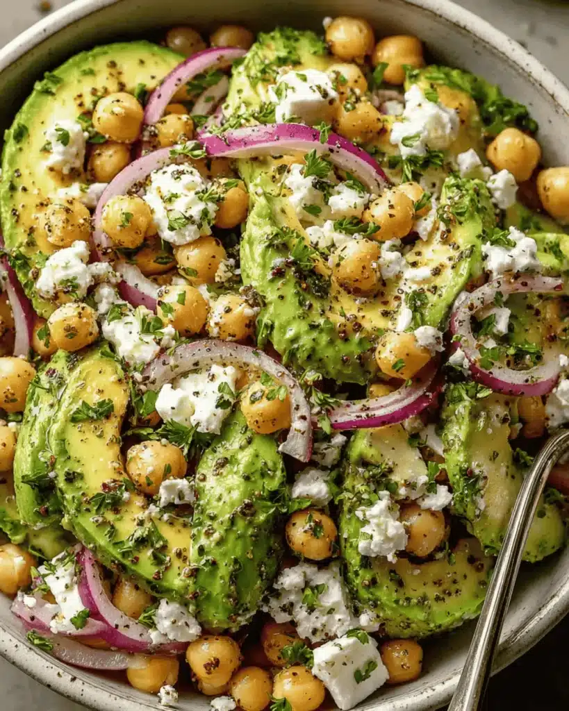 Mediterranean avocado chickpea salad with feta cheese, red onion, and parsley in a ceramic bowl