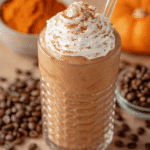 Pumpkin spice latte protein shake topped with whipped cream in a ribbed glass surrounded by coffee beans