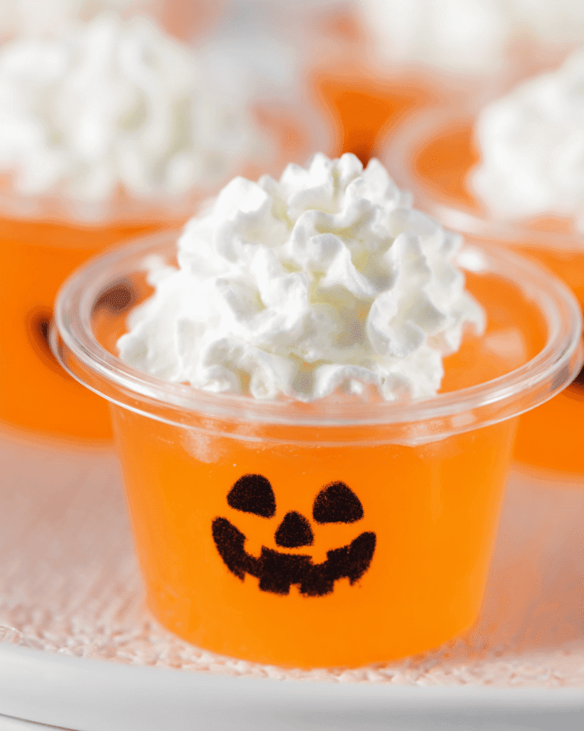 Close-up of Jack-O-Lantern keto jello shot with whipped cream topping in a clear cup