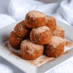 Keto pumpkin pie fat bombs stacked on a white plate, dusted with cinnamon sugar for a festive low carb holiday dessert