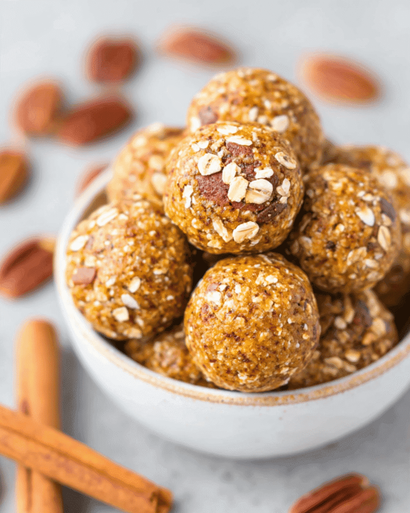 Bowl of no bake pumpkin energy balls with oats, pecans, and cinnamon sticks on a light background.