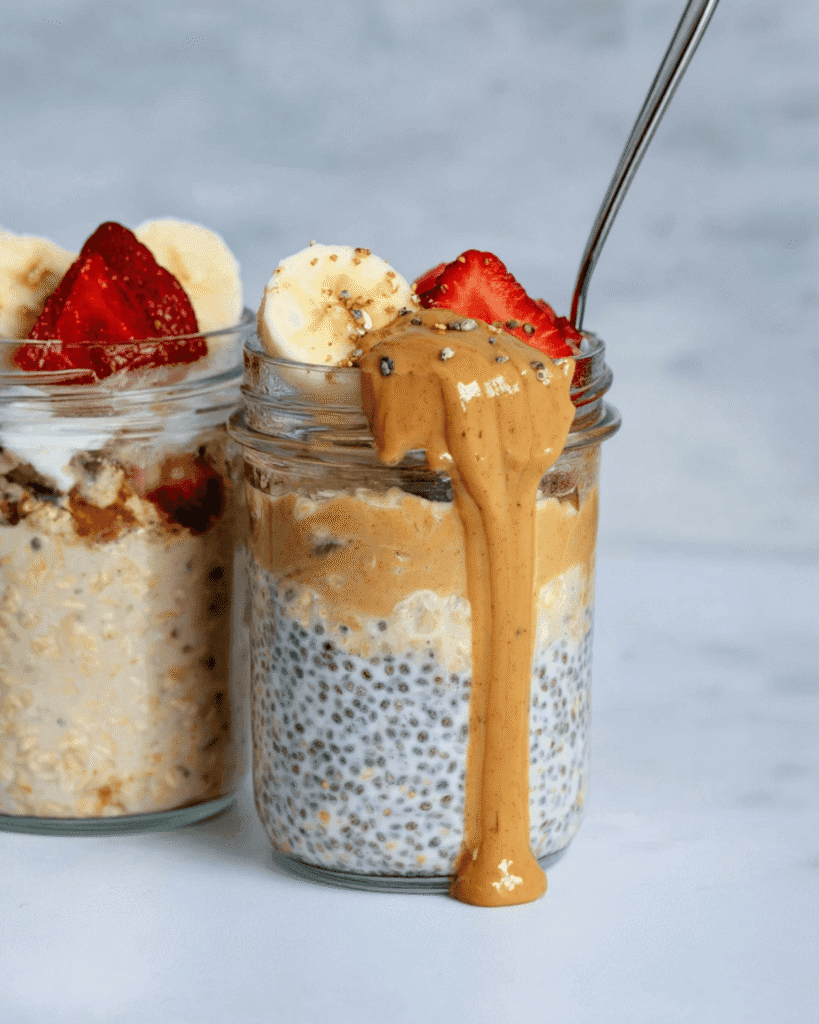 Overnight oats in glass jars with banana slices, strawberries, and peanut butter drizzle