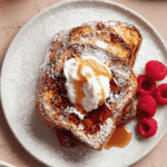 High protein French toast with whipped cream, maple syrup, and fresh raspberries on a white plate