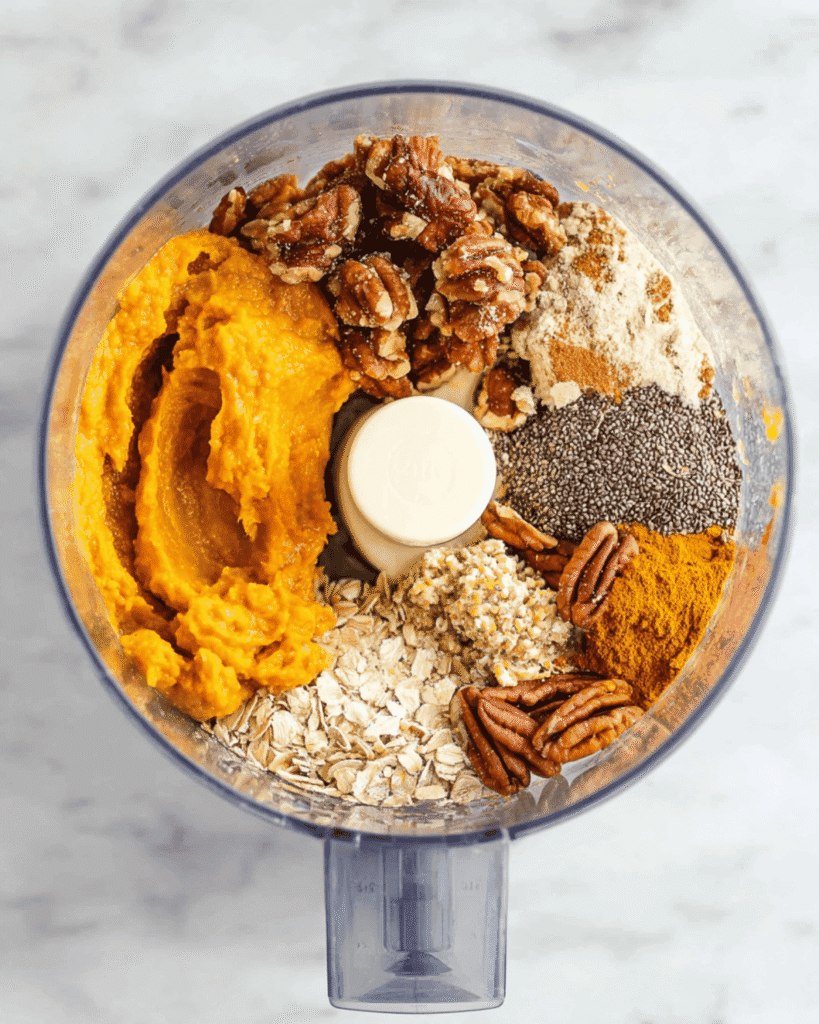 Food processor filled with pumpkin puree, oats, pecans, chia seeds, and spices for no bake pumpkin energy balls.