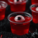 Close-up of Halloween eyeball jello shot with candy eyeball and plastic spider decoration on a dark background.
