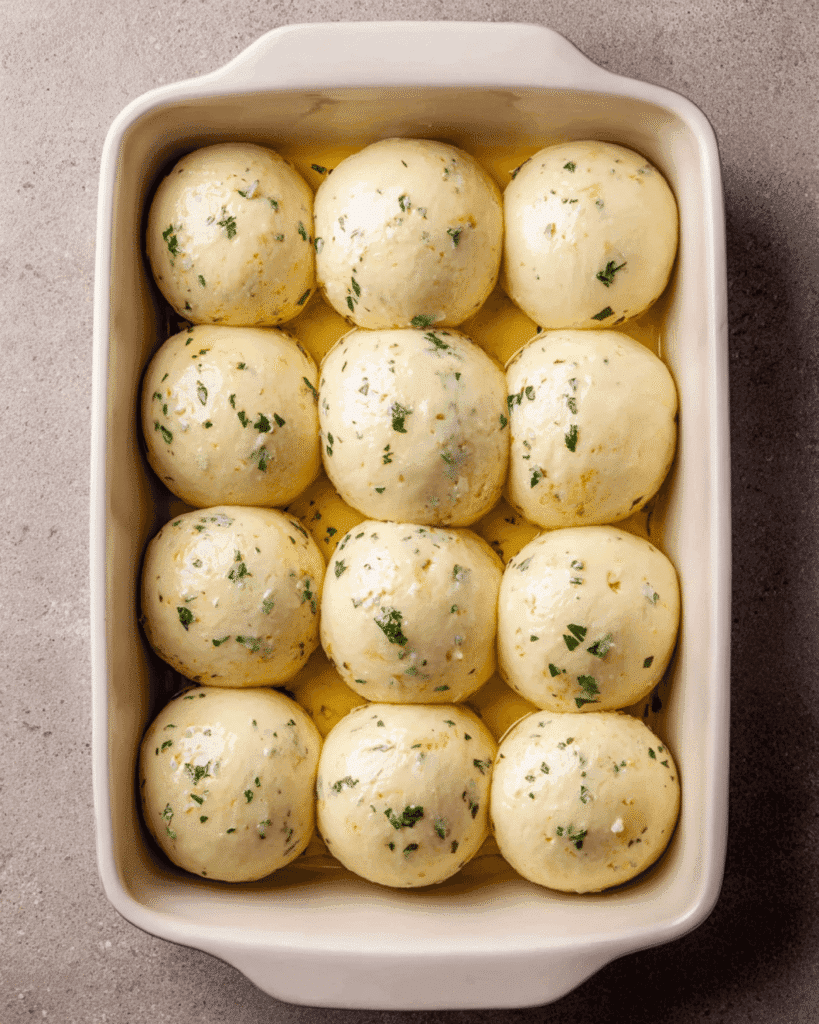 Garlic bread rolls dough proofing in a white baking dish with parsley and butter