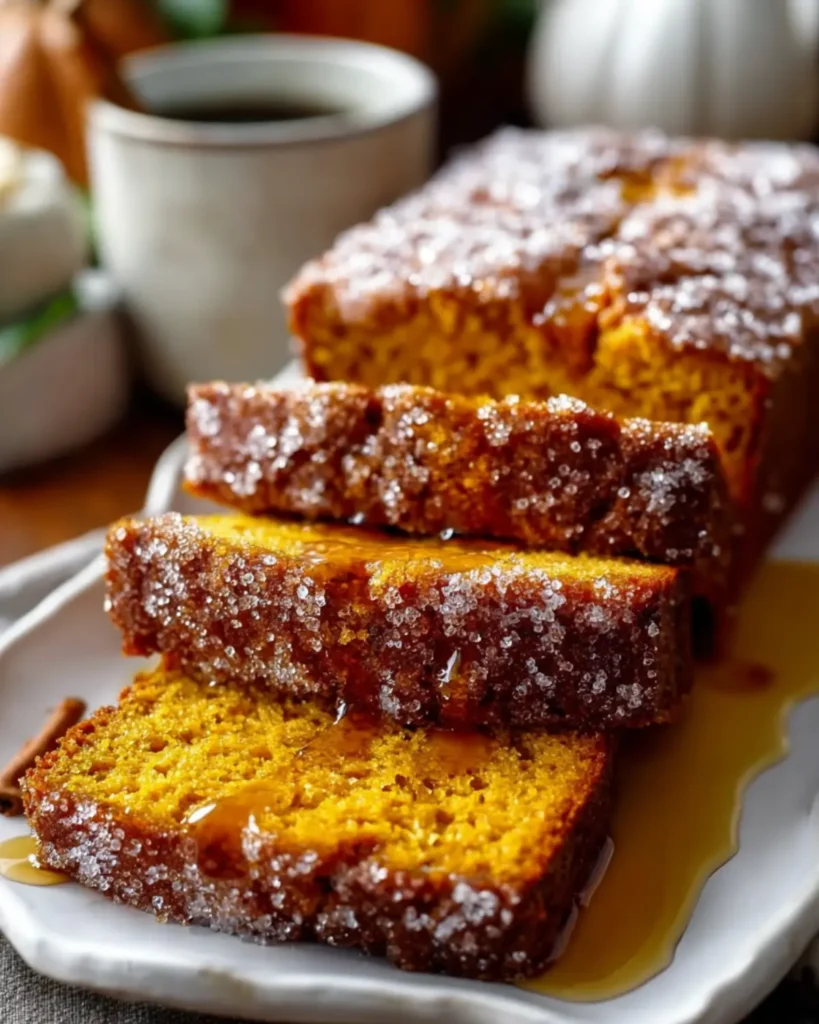 Close-up of moist pumpkin bread slices topped with cinnamon sugar and syrup drizzle on a white plate
