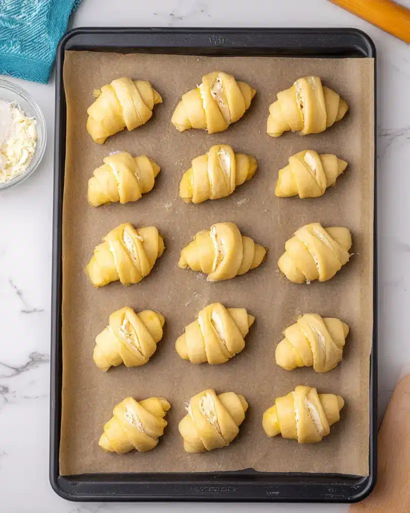 Unbaked crescent rolls filled with brie and pear neatly arranged on a parchment-lined baking tray.