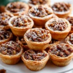 Freshly baked pecan tassies dusted with powdered sugar on a white serving stand.