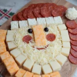 Finished Santa cheese board with pepperoni hat, olive eyes, and shredded cheese beard on wooden board