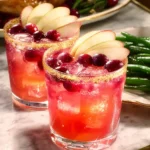 Thanksgiving Margarita cocktail with cranberries and apple slices on a marble table, garnished with a cinnamon sugar rim