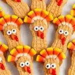 Peanut-shaped Nutter Butter turkey cookies decorated with candy corn feathers, candy eyes, and red icing on a white background.