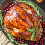 Golden brown maple-glazed Thanksgiving turkey surrounded by fresh rosemary and cranberries on a festive serving platter.