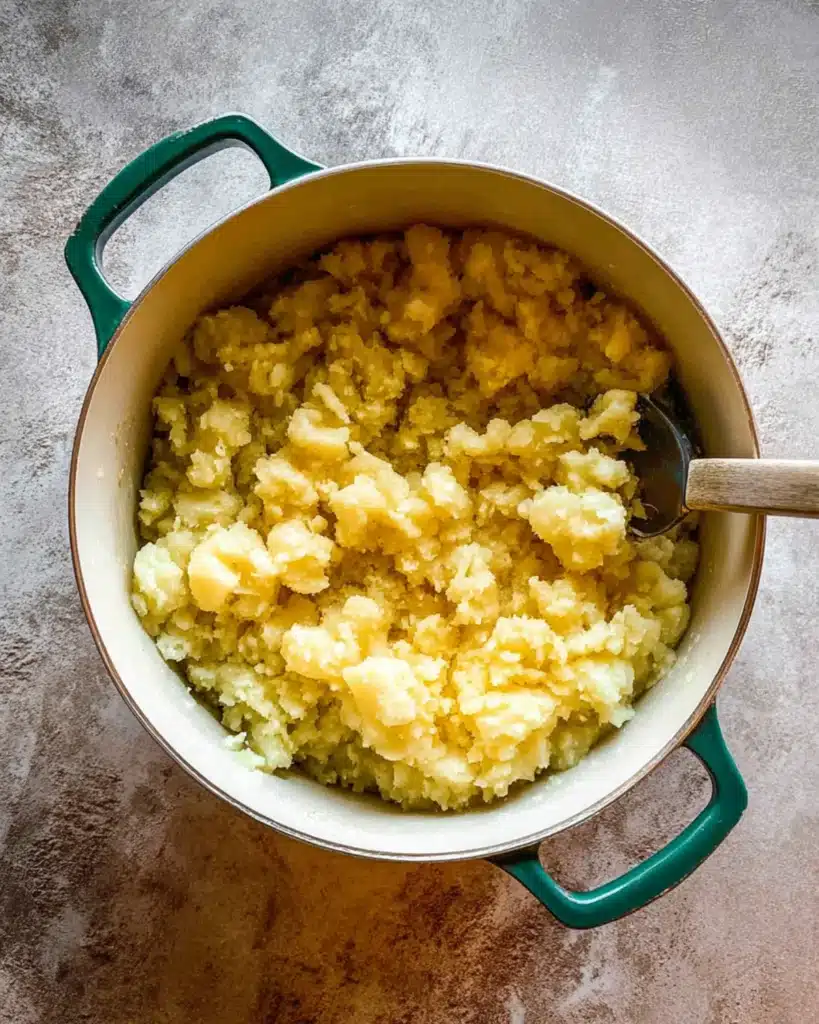 Overhead view of Yukon Gold potatoes partially mashed in a pot for creamy roasted garlic mascarpone mashed potatoes