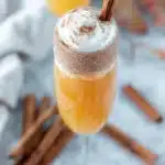 Pumpkin Pie Mimosa cocktail in a champagne flute topped with whipped cream and a cinnamon stick