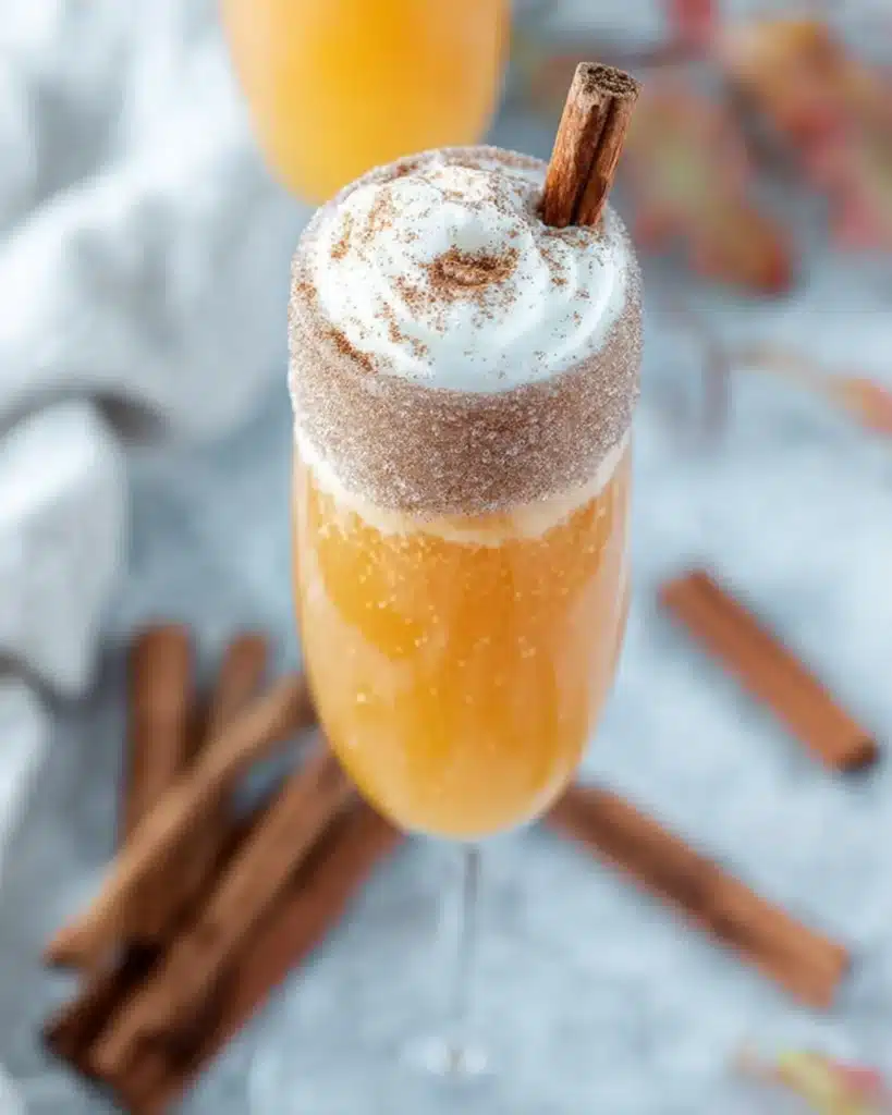 Pumpkin Pie Mimosa cocktail in a champagne flute topped with whipped cream and a cinnamon stick