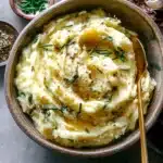Creamy roasted garlic mascarpone mashed potatoes topped with chives and cracked pepper in a rustic bowl