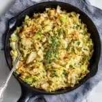 Cast iron skillet filled with sauteed cabbage and thyme on a gray striped napkin