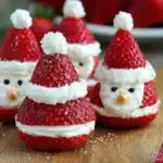 Close-up of strawberry Santas made with whipped cream filling, arranged on a wooden board for a festive Christmas dessert.