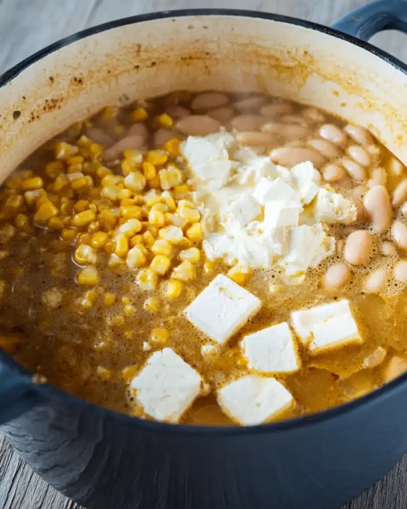 White chicken chili ingredients in a pot with beans, corn, and melting cream cheese.