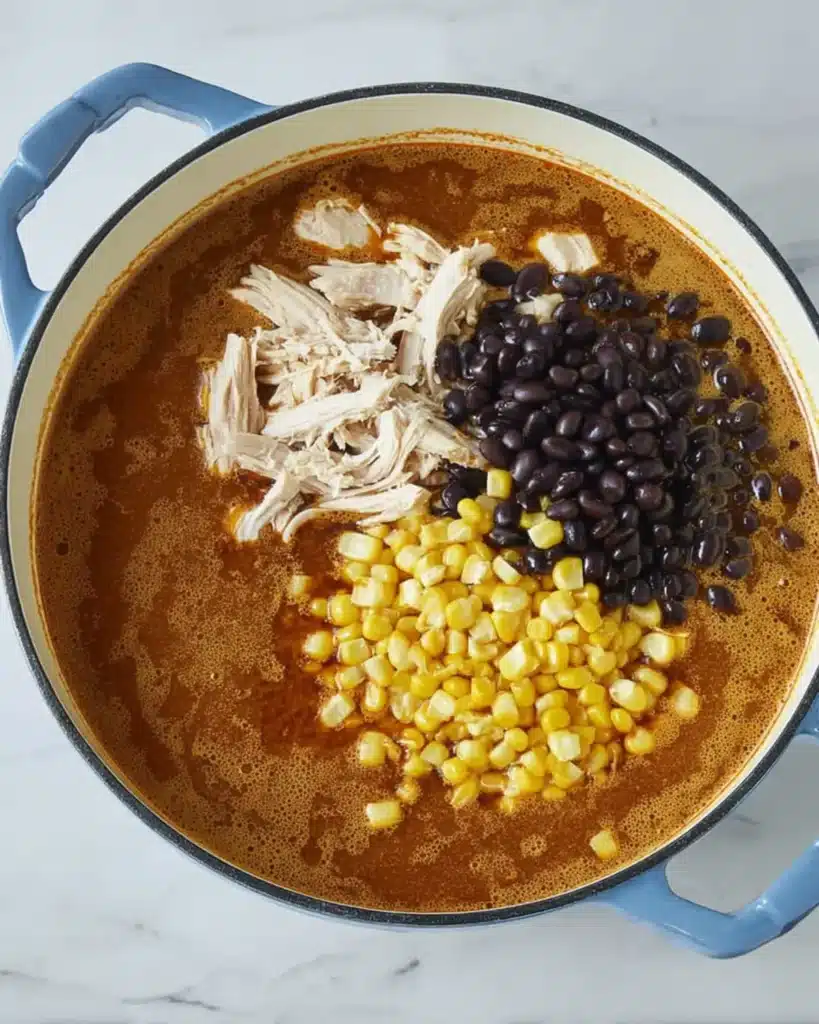 Overhead shot of chicken, corn, and black beans simmering in a flavorful tomato broth inside a Dutch oven for Chicken Tortilla Soup.