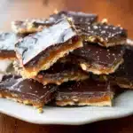 Stacked pieces of Christmas Crack recipe candy with chocolate and caramel layers on a white plate