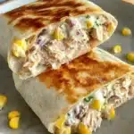 Golden grilled tuna melt wrap cut in half on a plate with creamy tuna and corn filling.